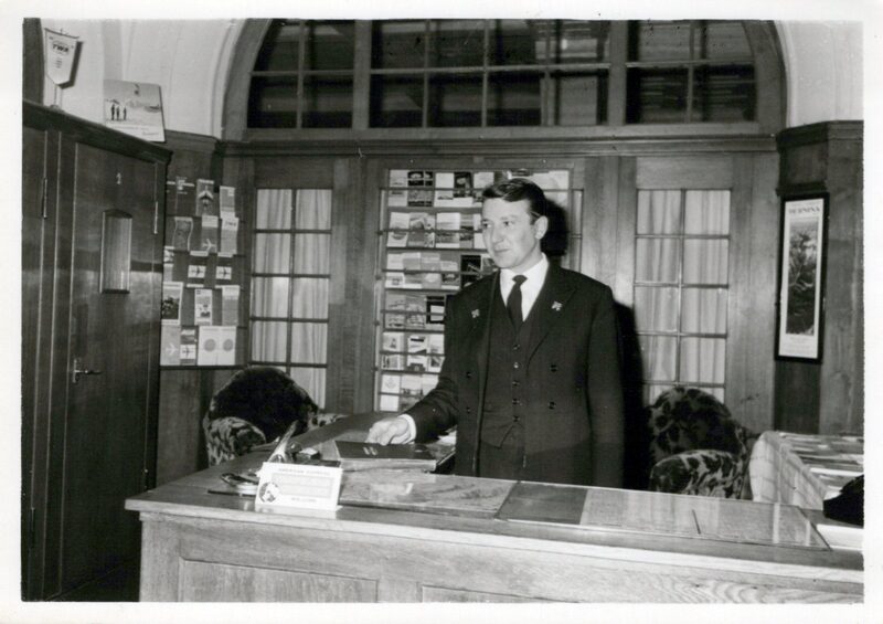 Sepp am Concierge-Pult mit American-Express-Schild und TWA-Wimpel